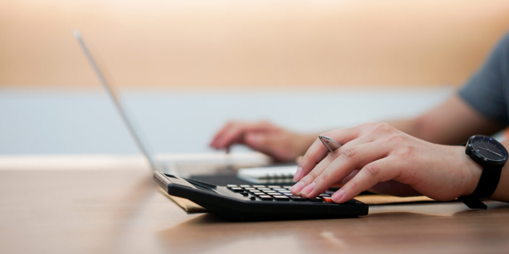 An accountant using a calculator beside a laptop