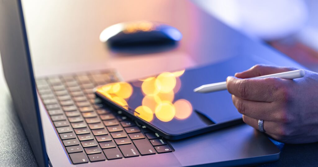 Hand using a stylus on a digital tablet beside a laptop